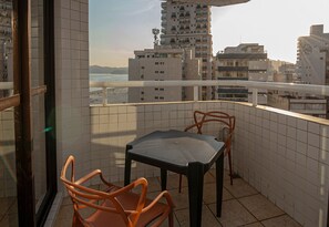 A balcony with a table and two chairs, overlooking a beach and city buildings. - SHB - Santos Living • Pool, Gym, and Sea View (Santos)