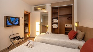 Een hotelkamer met twee bedden, een televisie, een kledingkast en een badkamer die door een open deur zichtbaar is.