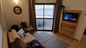Ein Wohnzimmer mit einer Couch, einem gemusterten Teppich, einem Fernseher und Blick durch ein großes Fenster.