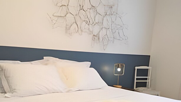 Un lit bien fait, avec du linge de lit blanc et une serviette enroulée, une tête de lit en bois et un luminaire fixé au mur.