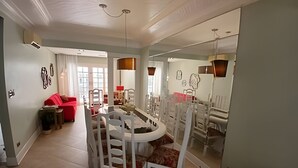 Un coin repas avec une table et des chaises blanches, un canapé rouge et un miroir qui reflète la pièce.