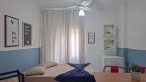 Ein Schlafzimmer mit Bett, Schreibtisch, Stuhl, Deckenventilator und einem Fenster mit Vorhängen.