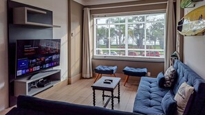 Una sala de estar moderna con un televisor de pantalla plana, un sofá, una mesa de centro y un ventanal con vistas al exterior.