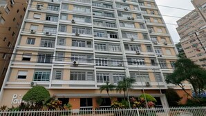 Un edificio residencial de varios pisos con fachada uniforme, unidades de aire acondicionado y entrada protegida con área ajardinada.