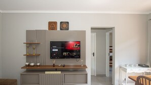 A living room with a flat-screen TV, wooden entertainment unit, and a sign that reads 'WELCOME TO THE TIKI BAR'. - SHB - Happy family: Fast Wi-Fi 1 minute from the beach (São Vicente)