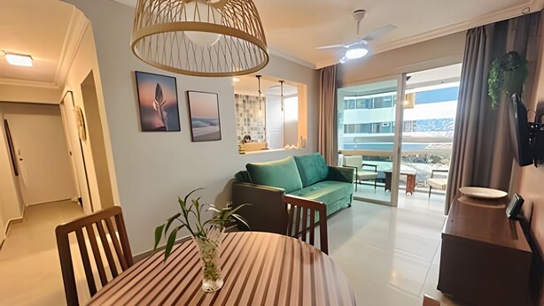 A modern living room with a round wooden table, a green sofa, and a dining area. - SHB - The Best of Pitangueiras with Beach Service (Guarujá)