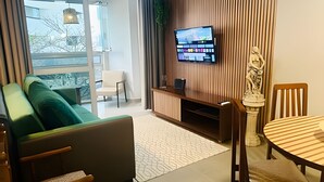 A modern living room with a sofa, a dining table, and a TV mounted on a wooden wall. - SHB - The Best of Pitangueiras with Beach Service (Guarujá)