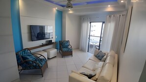 Ein modernes Wohnzimmer mit Flachbildfernseher, einer Couch, zwei Sesseln und einem Couchtisch.