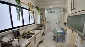 Eine moderne Küche mit Gasherd, Spüle und Mikrowelle. Über den Fenstern hängen Pflanzen und es gibt einen kleinen Essbereich mit Hocker.