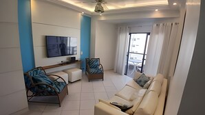 Ein modernes Wohnzimmer mit einer Couch, zwei Sesseln, einem an der Wand befestigten Fernseher und einem Balkon mit Blick.