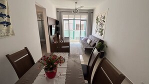 Un área de comedor con una mesa preparada para dos personas, un sofá y un televisor al fondo.