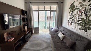 Una sala de estar con televisor, sofá y un ventanal con cortinas.