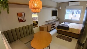 Un espace de vie compact comprenant un canapé, une petite table ronde, un lit, un téléviseur et une fenêtre donnant sur un beau paysage.