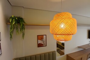 Ein modernes Interieur mit einer hängenden, orangefarbenen Pendelleuchte, einer Zimmerpflanze und einem gerahmten Kunstwerk an der Wand.