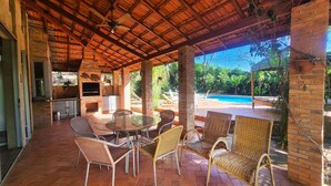 Une terrasse extérieure avec un sol en briques, des meubles en osier et une piscine en arrière-plan.