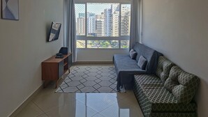 A modern living room with a sofa, a small wooden table, a TV, and a large window with a city view.
