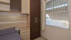 A bedroom with a bed, a wardrobe, a window with a view of the beach, and a balcony.