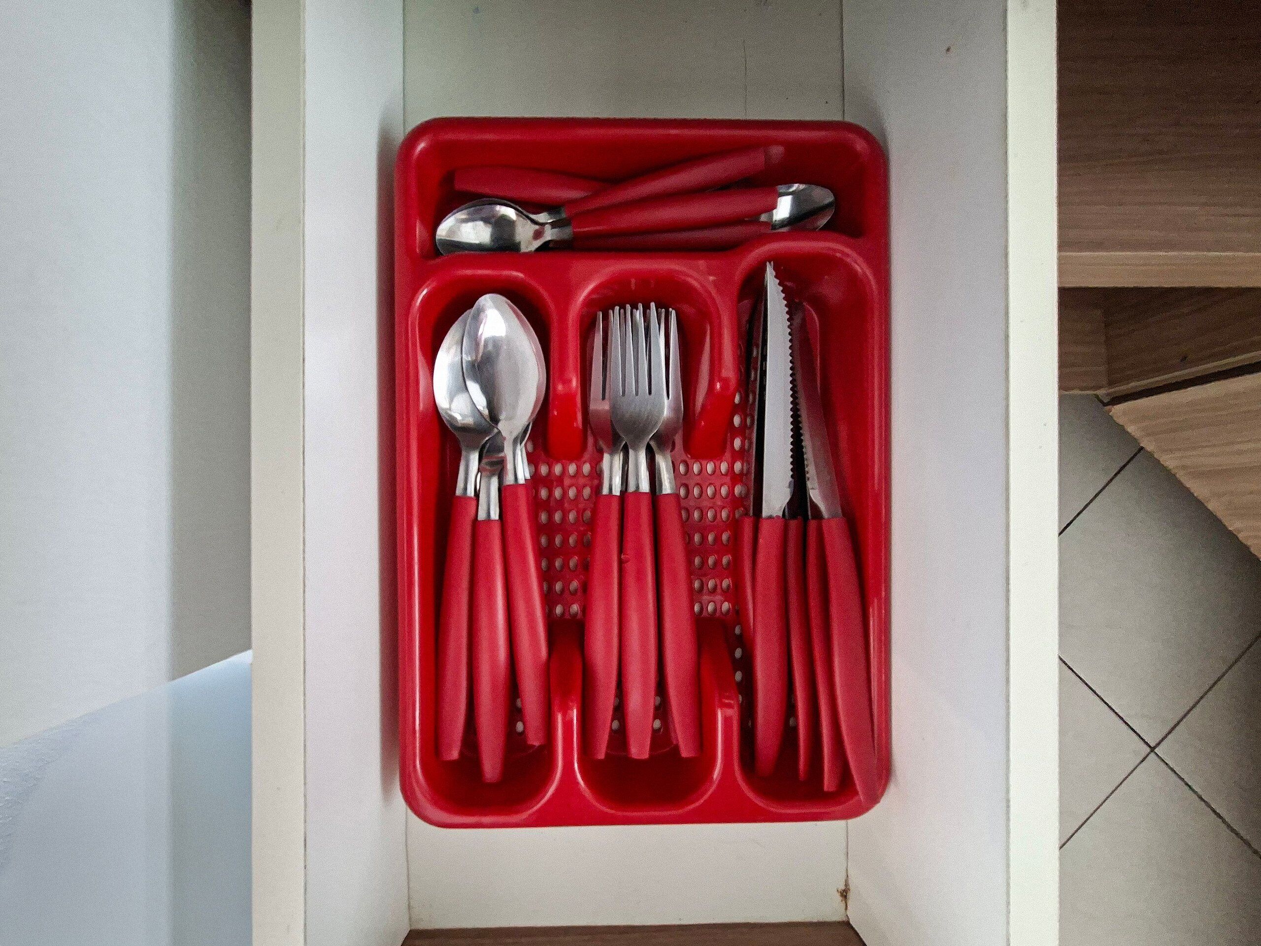 Suporte vermelho para utensílios com colheres, garfos e faca dentro de um armário.