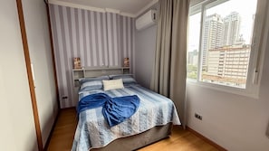Ein Schlafzimmer mit Bett, gestreifte Vorhänge, einem Fenster mit Blick auf die Stadt und einer Klimaanlage.