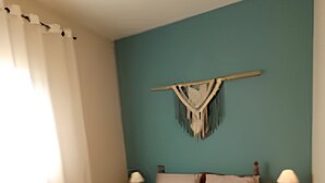 Ein Schlafzimmer mit einem Bett, zwei Nachttischen, einer Wanddekoration und einem Fenster mit Vorhängen.