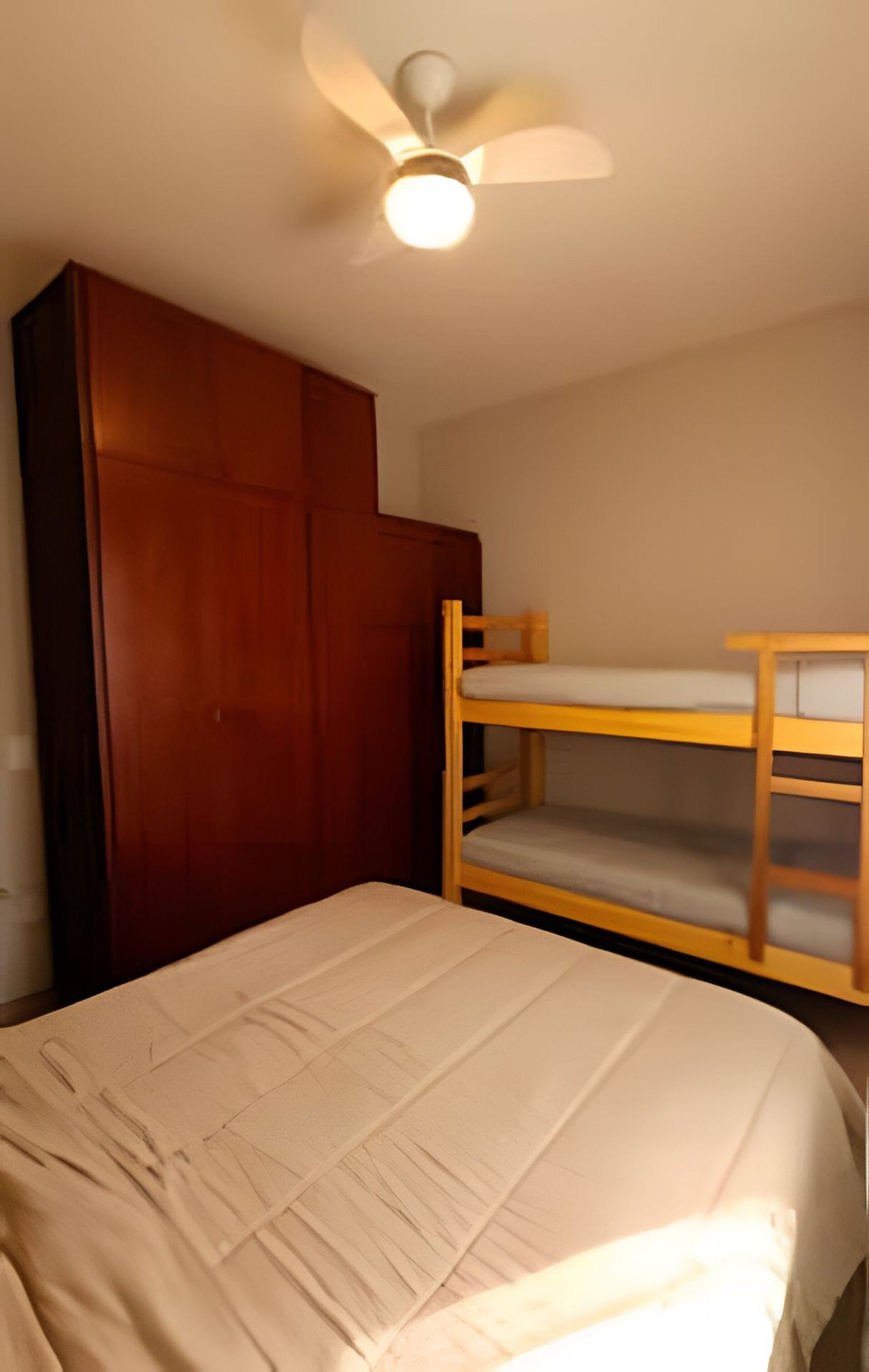 Un dormitorio con una cama litera, un armario de madera y un ventilador de techo.
