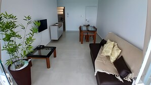 A living room with a sofa, a coffee table, a TV, and a dining area with a table and chairs. - SHB - Amazing view | On the Sand | Pitangueiras (Guarujá)