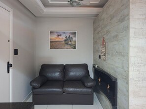 A room with a black leather sofa, a fireplace, a wall-mounted picture, and a ceiling fan.