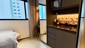 Una camera d'albergo compatta con un letto, angolo cottura e finestra vista su un edificio.