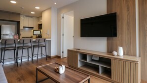 Uma sala de estar moderna com televisão de tela plana, móvel para entretenimento em madeira e área de cozinha com banquetas.