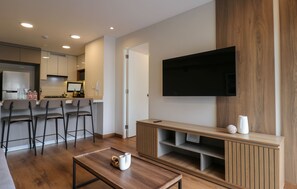 Ein modernes Wohnzimmer mit Flachbildfernseher, einer Holzunterhaltungsecke und einer Küchenzeile mit Barhocker.