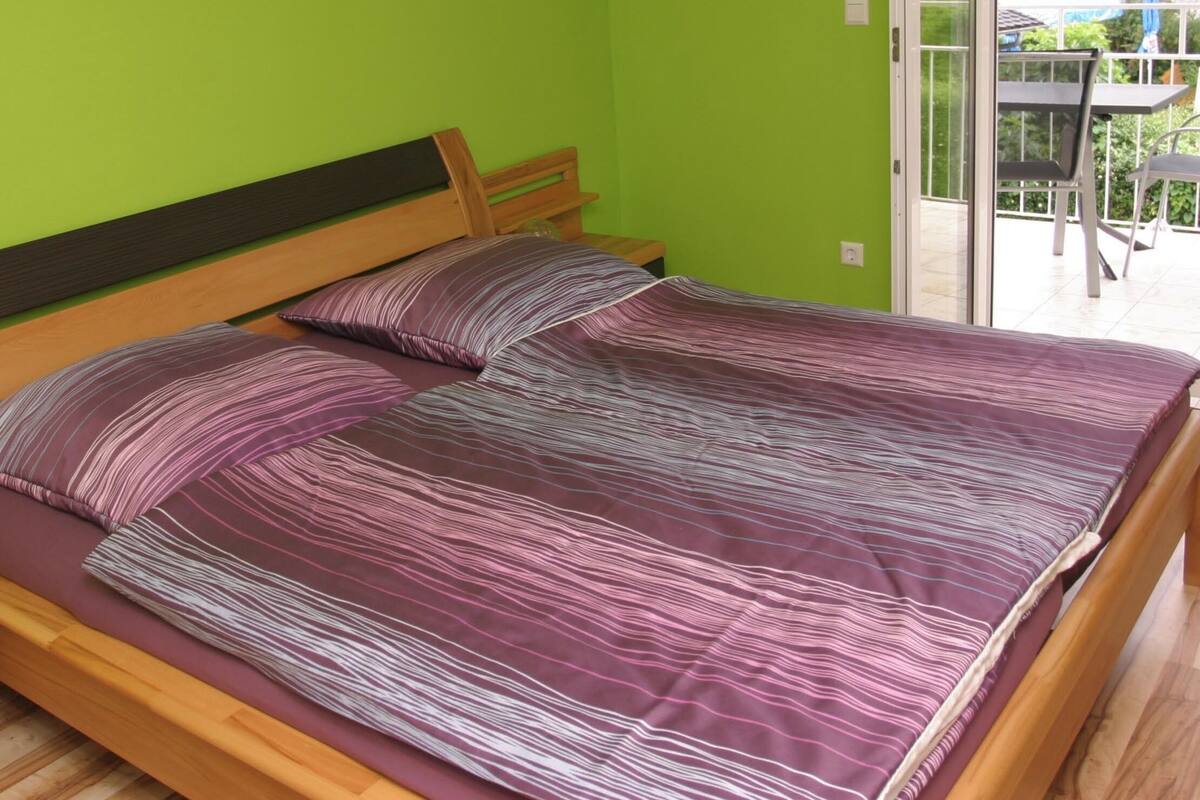 Ein Doppelbett mit Holzrahmen und einer violett-gestreiften Bettdecke in einem Zimmer mit grünen Wänden.