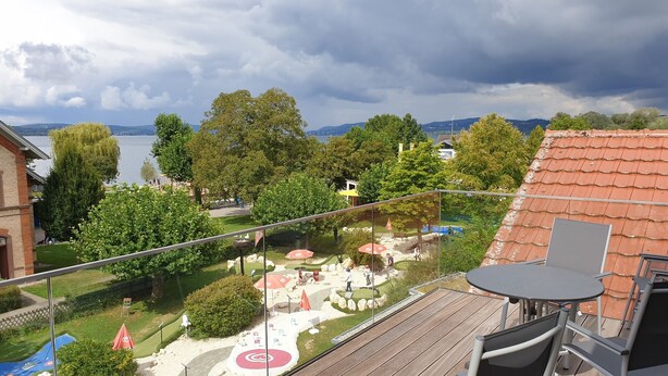 A balcony with a view of a landscaped garden, a pool area, and a lake. - Pension Antje Ekert (Uhldingen-Muehlhofen)