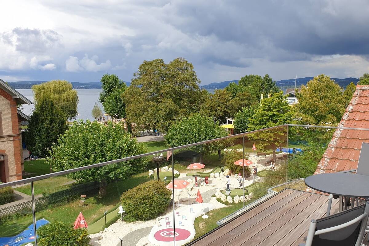 Ein Balkon mit Blick auf einen angelegten Garten, einen Poolbereich und einen See.