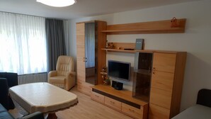 A living room with a sofa, a chair, a TV, a wooden cabinet, and a table. - Pension Antje Ekert (Uhldingen-Muehlhofen)