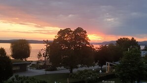 A sunset view over a lake with trees and a park area in the foreground. - Pension Antje Ekert (Uhldingen-Muehlhofen)