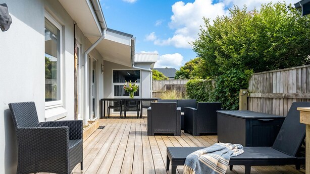 Une terrasse en bois, aménagée avec du mobilier d’extérieur, notamment des chaises et une table, et offrant une vue sur une maison dotée d’une fenêtre et d’une porte.