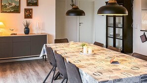 Un coin repas avec une table dressée pour quatre personnes, deux lampes suspendues, un buffet et une porte en arrière-plan.