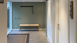 Un couloir avec un banc, un luminaire fixé au mur et une porte ornée d’un panneau décoratif.