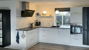 Une cuisine moderne avec des meubles blancs, un plan de travail noir, un four encastré et une fenêtre donnant sur l’extérieur.