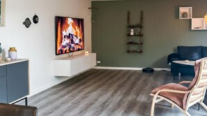 Un salon moderne doté d’un téléviseur à écran plat, d’un mur d’accent de couleur vert foncé, d’un plancher en bois et d’un canapé en cuir.