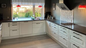 A modern kitchen with white cabinetry, a black countertop, and a view of the garden through the window. - 3 bedroom cozy home in Bøvlingbjerg (Bøvlingbjerg)