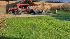 A building with a red-roofed structure, solar panels on the roof, and outdoor seating with chairs and tables. - 3 bedroom cozy home in Bøvlingbjerg (Bøvlingbjerg)