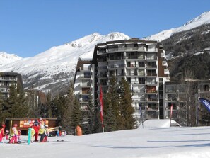 Ein mehrstöckiges Hotel mit Balkonen vor einer Kulisse schneebedeckter Berge.