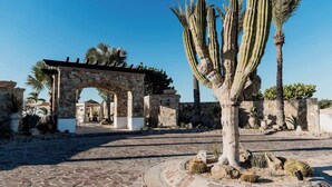 A stone archway leading to a courtyard with cacti and palm trees. - Golf & Beach Club Villa | Perfect for Families (Ciudad de los cabos)