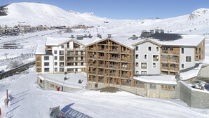 Un hôtel à plusieurs étages, doté d’une façade en bois, de grandes fenêtres et, en arrière-plan, d’une piste de ski.