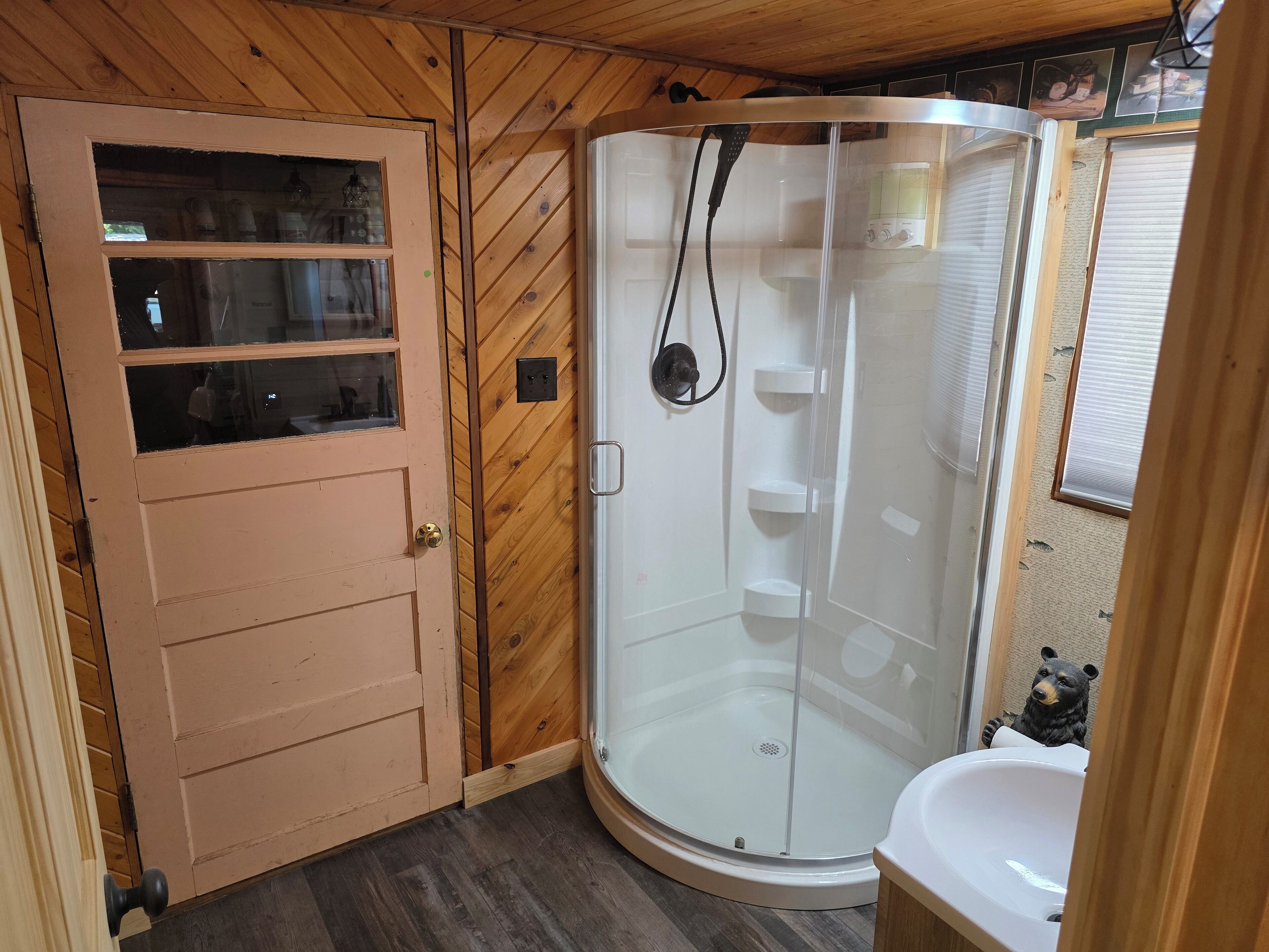 Une douche d’angle avec une porte en verre, une porte en bois avec des panneaux de verre et un lavabo blanc.