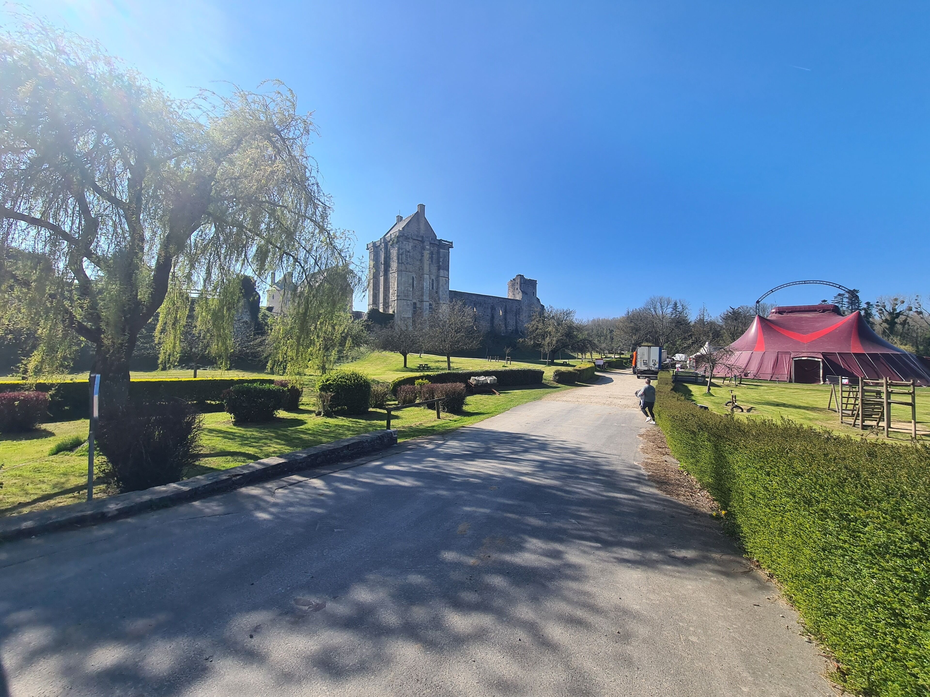 Ein Weg führt zu einem historischen Gebäude mit einem Turm, umgeben von gepflegten Gärten und einer roten Zelthalle.