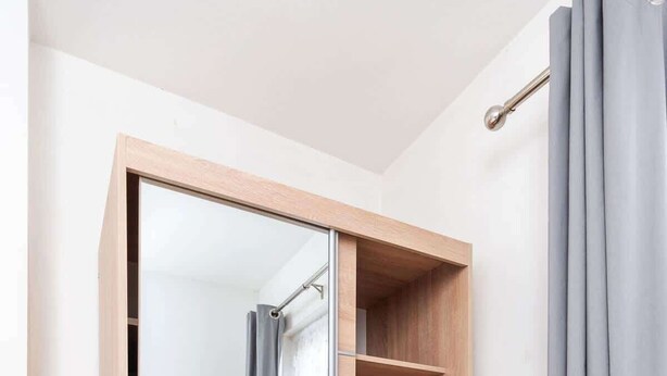 Ein begehbarer Kleiderschrank mit Spiegel, Holzböden und einem grauen Vorhang.