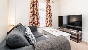 Ein Wohnzimmer mit einer Couch, einem Couchtisch, einem Fernseher und einem Fenster mit Vorhängen.