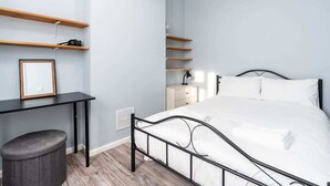 Ein Schlafzimmer mit einem Bett, einem Schreibtisch, Regalen und einem Mülleimer.